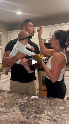 a man and woman standing in a kitchen with a baby eating out of a bowl