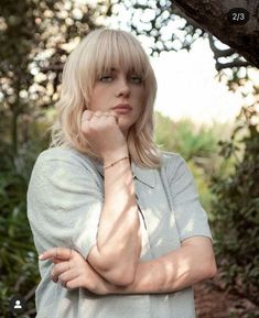 a woman standing in front of a tree with her hand on her chin and looking at the camera