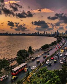 a city street filled with lots of traffic next to the ocean under a cloudy sky