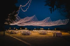 an outdoor event with tables and chairs covered in white tablecloths, lit by fairy lights