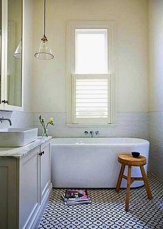 a white bath tub sitting under a window next to a sink and counter with a stool