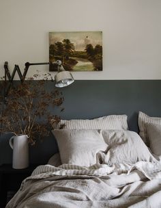 an unmade bed with white linens and pillows in front of a painting on the wall