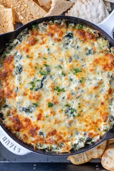 spinach dip in a cast iron skillet surrounded by crackers and tortilla chips