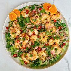 a white plate topped with salad and shrimp next to an orange slice on top of it