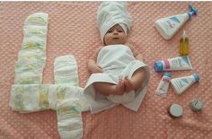 a baby laying on top of a pink blanket next to bottles and other items that include toothpaste