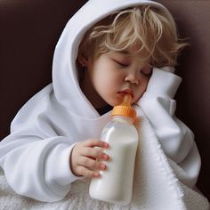 a young child in a white robe is drinking from a bottle while wrapped in a blanket