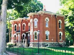 an old red brick house in the middle of a tree lined park with lots of green grass