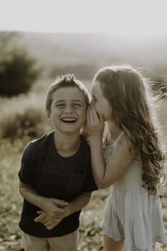 two young children standing next to each other in a field with grass and trees behind them