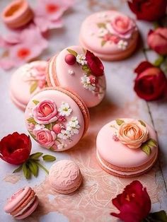 pink macaroons decorated with flowers and leaves on a table next to red roses