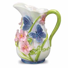 a glass pitcher with flowers and butterflies painted on the side, sitting in front of a white background