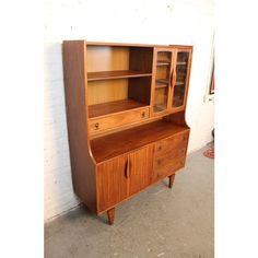 a wooden cabinet with glass doors and drawers on the front, against a white brick wall