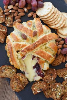 a blue plate topped with bread and crackers next to grapes, nuts and cheese