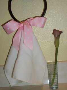 a pink rose in a glass vase with a ribbon on it and a towel hanging from the handle