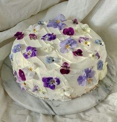 a cake with white frosting and purple pansies on it sitting on a marble platter