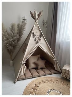 a teepee tent with pillows on the floor next to a rug and potted plant