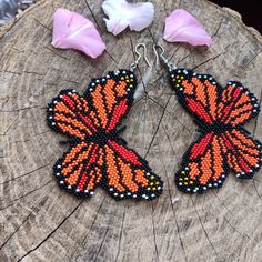 a pair of orange and black beaded butterfly earrings sitting on top of a tree stump