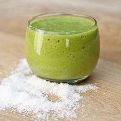 a green smoothie in a small glass on top of a wooden table with the words clean eating written above it