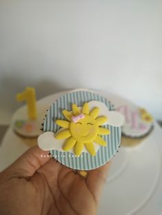 a hand holding a cupcake decorated with the number 1 and sunflowers on it