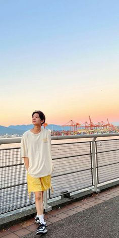 a man standing on the side of a road next to a body of water at sunset