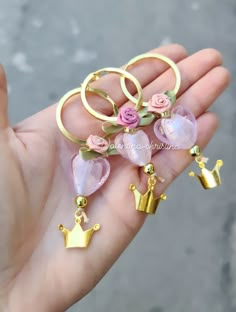 a person is holding several rings with pink flowers on them and two gold crowns hanging from them