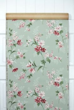 a wall hanging on the side of a white brick wall next to a green and pink flowered curtain