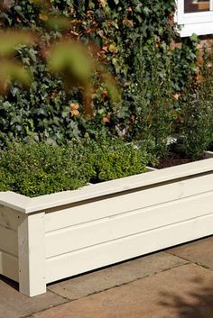 a white planter sitting on top of a sidewalk next to a brick wall and bushes