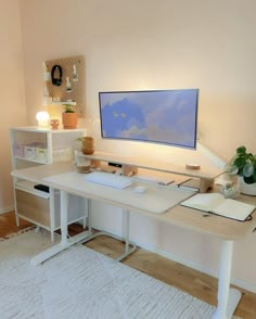 a white desk with a computer on it and a plant in front of the monitor