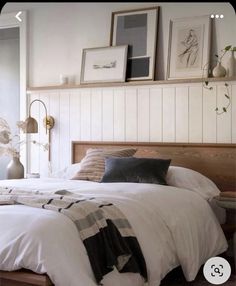 a bed with white sheets and pillows in a bedroom next to a window filled with pictures