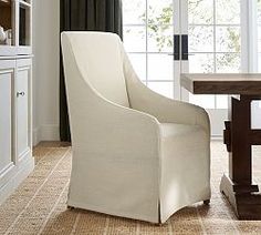 a white chair sitting in front of a window next to a wooden table and chairs