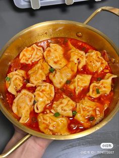 a person holding a pan filled with dumplings in tomato sauce on top of a table