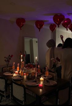 a group of people standing around a dining room table with candles and heart shaped balloons