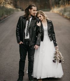 a man and woman standing next to each other on a road with trees in the background