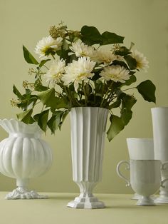 white vases with flowers in them sitting on a table next to cups and saucers