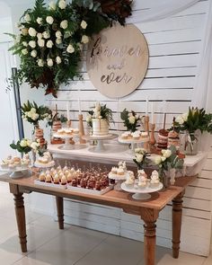 a table topped with cakes and cupcakes on top of wooden tables covered in greenery