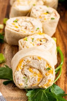 chicken salad wrapped in bread on a cutting board with green leaves around it and another wrapper next to it