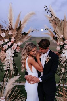 a bride and groom standing in front of a floral arch