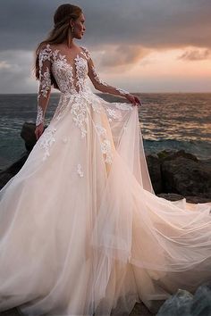 a woman in a wedding dress standing on the rocks by the ocean with her back to the camera