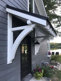 a gray house with white trim on the front door and side porch, along with potted plants