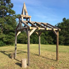 a wooden structure sitting in the middle of a grass covered field with trees behind it