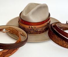 We partnered with our favorite local leather artisan to bring you an exclusive line of one-of-a-kind handmade Western hat bands repurposed from soft & worn vintage leather belts Hat bands are adjustable with a leather cord from about 21-3/4" to 24-1/4" Available in 8 styles (numbered from top-to-bottom): STYLE #1: Two tone brown leather band with stamped leaf & flower accents and tan leather adjuster.  Width: 5/8" STYLE #2: Two tone brown hand finished top grain leather band with tan leather adj Cowboy Hat Band, American Vintage Clothing, Cowboy Hat Bands, Hat Bands, Chapeau Cowboy, Vintage Leather Belts, Leather Hat, Leather Artisan, Western Hats