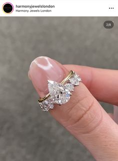 a woman's hand holding an engagement ring with three diamonds on it and the top half of her finger