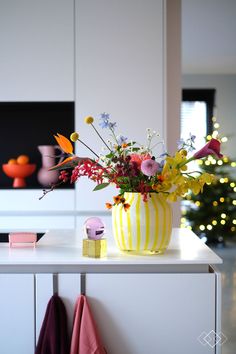 a vase filled with lots of flowers on top of a white counter next to a christmas tree