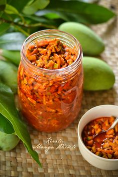 a jar filled with lots of food next to a bowl of sauce and some leaves