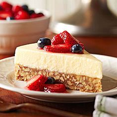 a piece of cheesecake on a plate with strawberries and blueberries in the background