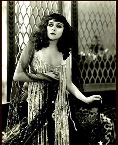 an old black and white photo of a woman wearing a fringed dress with her hands on her hips