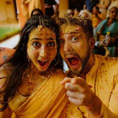 a man and woman covered in yellow paint pose for the camera while others look on