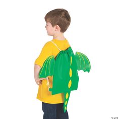 a young boy in a yellow shirt is holding a green dragon backpack and has it's wings folded over his shoulder