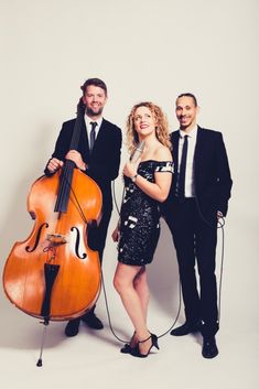 two men and a woman standing next to each other with a cello in front of them