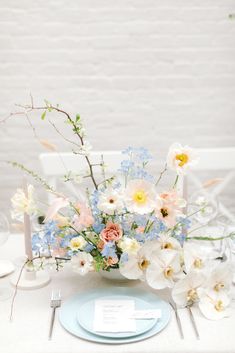 a white table topped with a blue plate and vase filled with different types of flowers