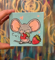 a hand holding up a small card with a drawing of a mouse eating a strawberry